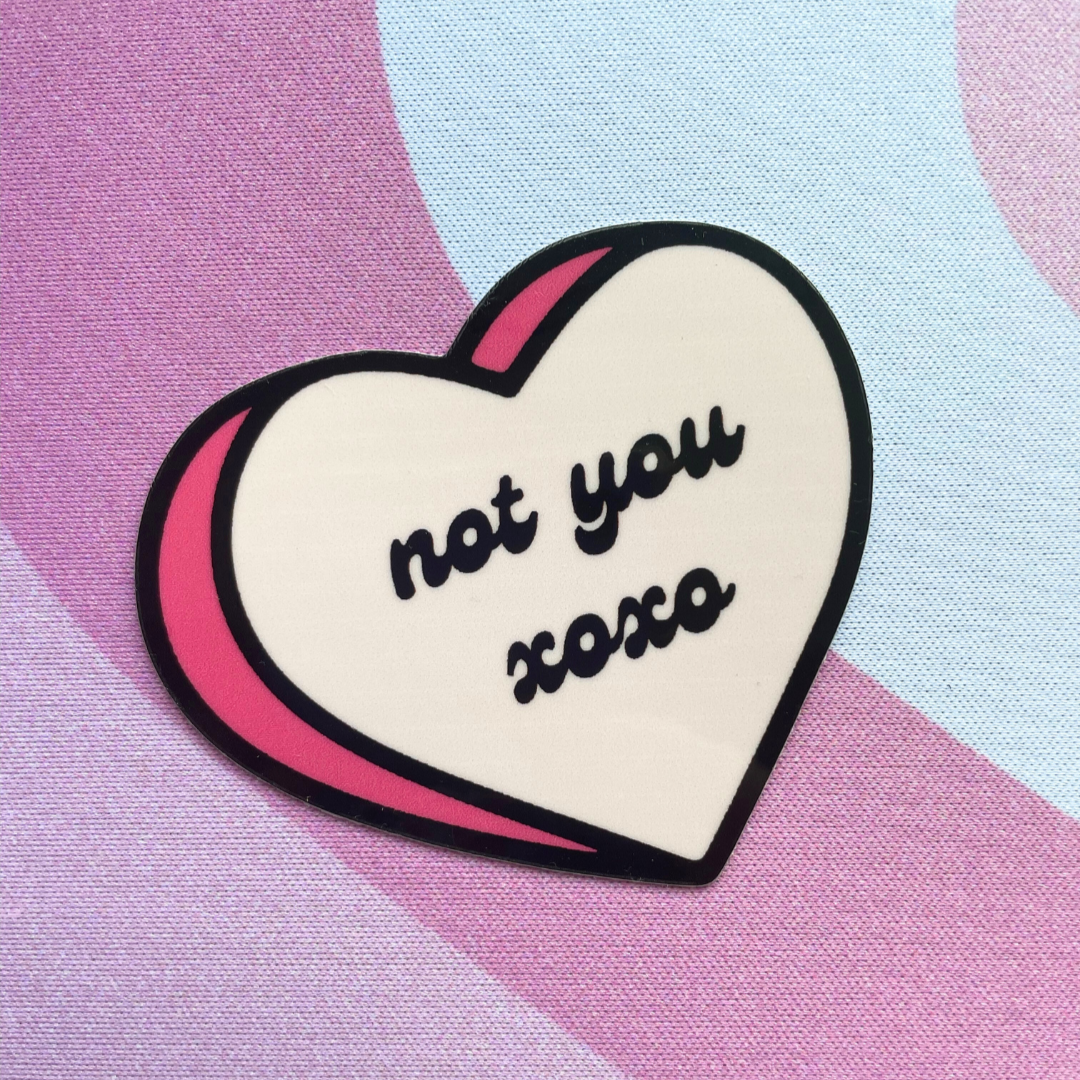 A die-cut sticker in the shape of a heart with the phrase 'not you xo' printed in black on a pink background.